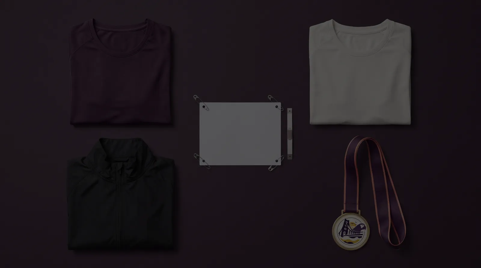 Kit de la carrera sobre una mesa color açaí: remera oficial violeta, remera finisher off-white, campera negra, número de pecho con chip y medalla